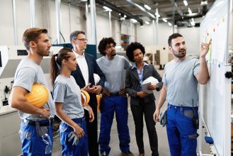 Happy manual worker presenting the results of business development while giving presentation to company leaders and his team in a factory.